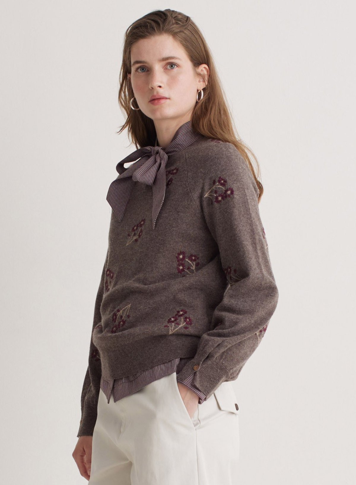 Woman wearing a brown sweater with floral embellishments on a white background