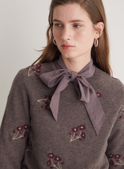 Woman wearing a brown sweater with floral embroidery and a purple bow