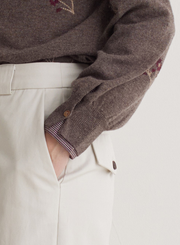 Close-up of a person wearing a brown jumper with floral embroidery and beige trousers.