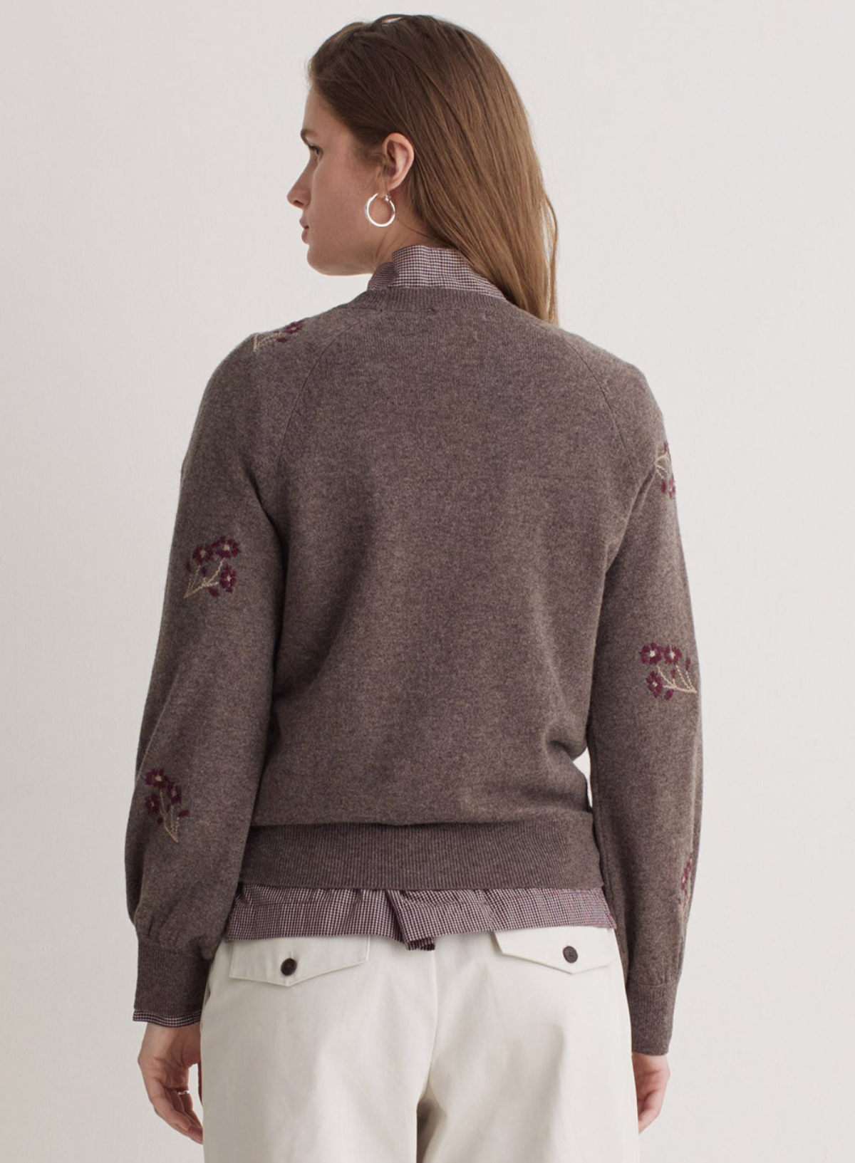 Person wearing a brown sweater with floral patterns on a plain background