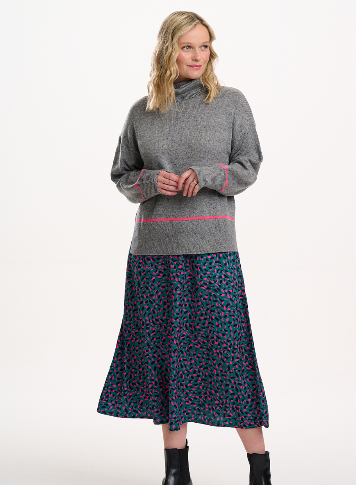 Woman wearing a gray sweater with pink accents and a patterned skirt on a white background