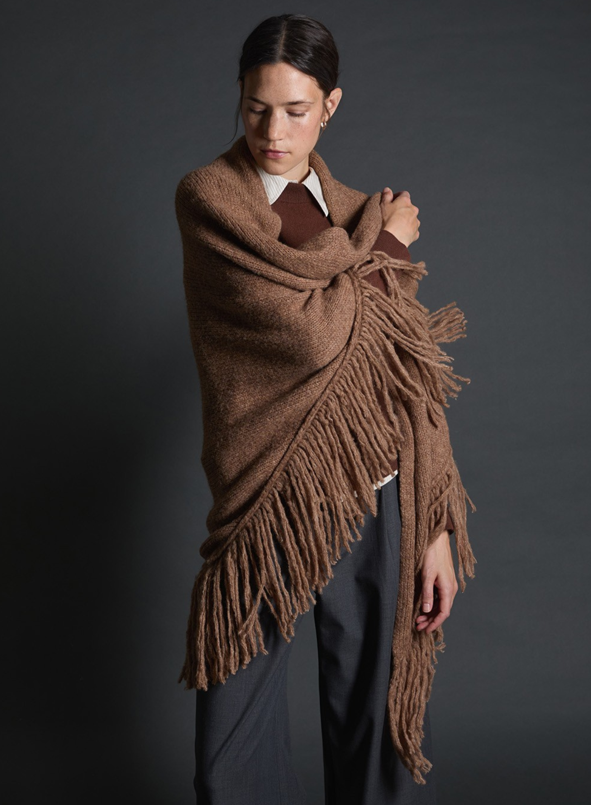 Woman wearing a brown fringed shawl against a dark background