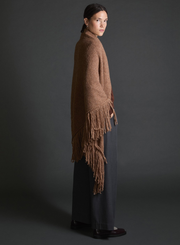 Person wearing a brown fringed shawl against a dark background