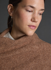 Close-up of a person wearing a brown knitted shawl against a gray background