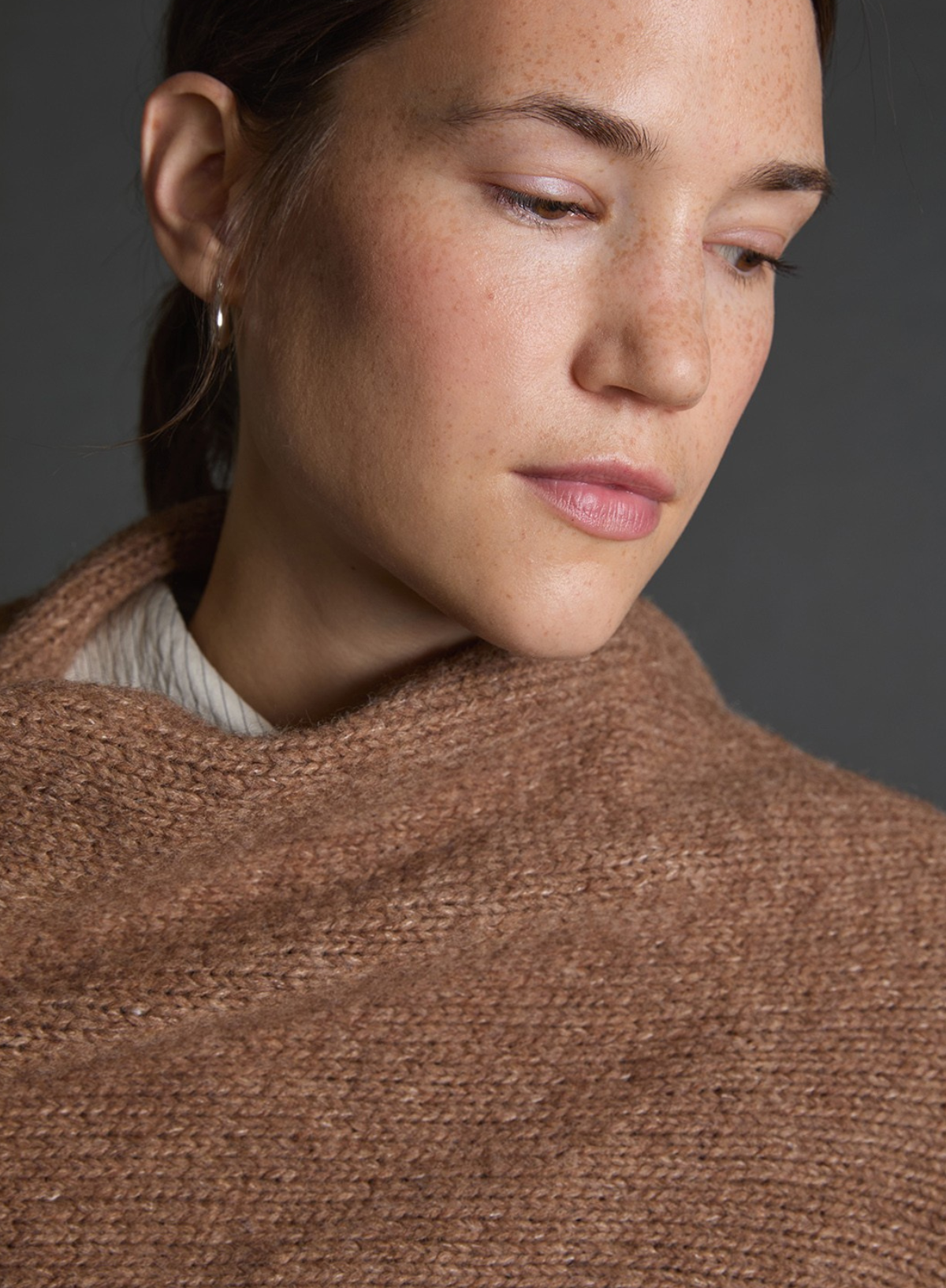 Close-up of a person wearing a brown knitted shawl against a gray background