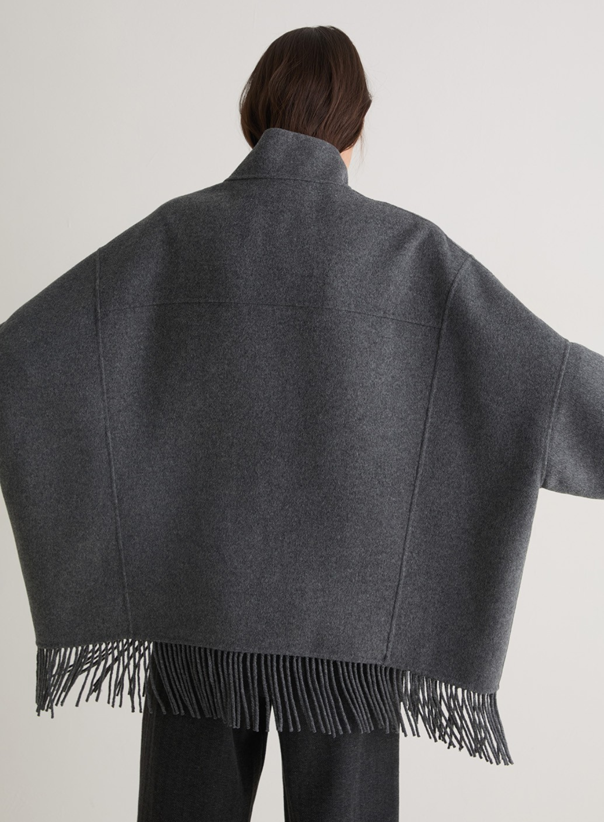 Person wearing a gray coat with fringes on a plain background