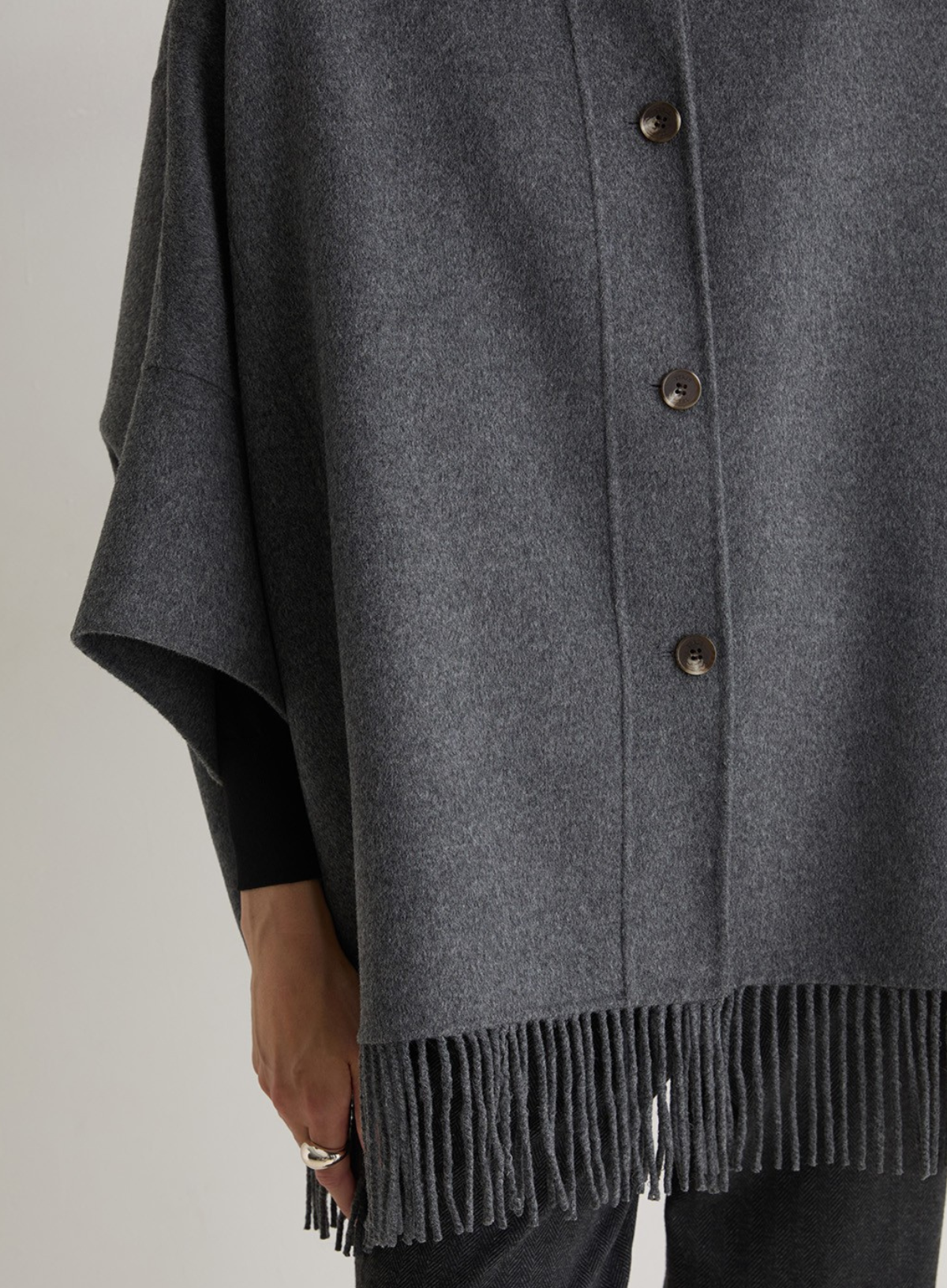 Gray poncho with fringes and buttons on a neutral background