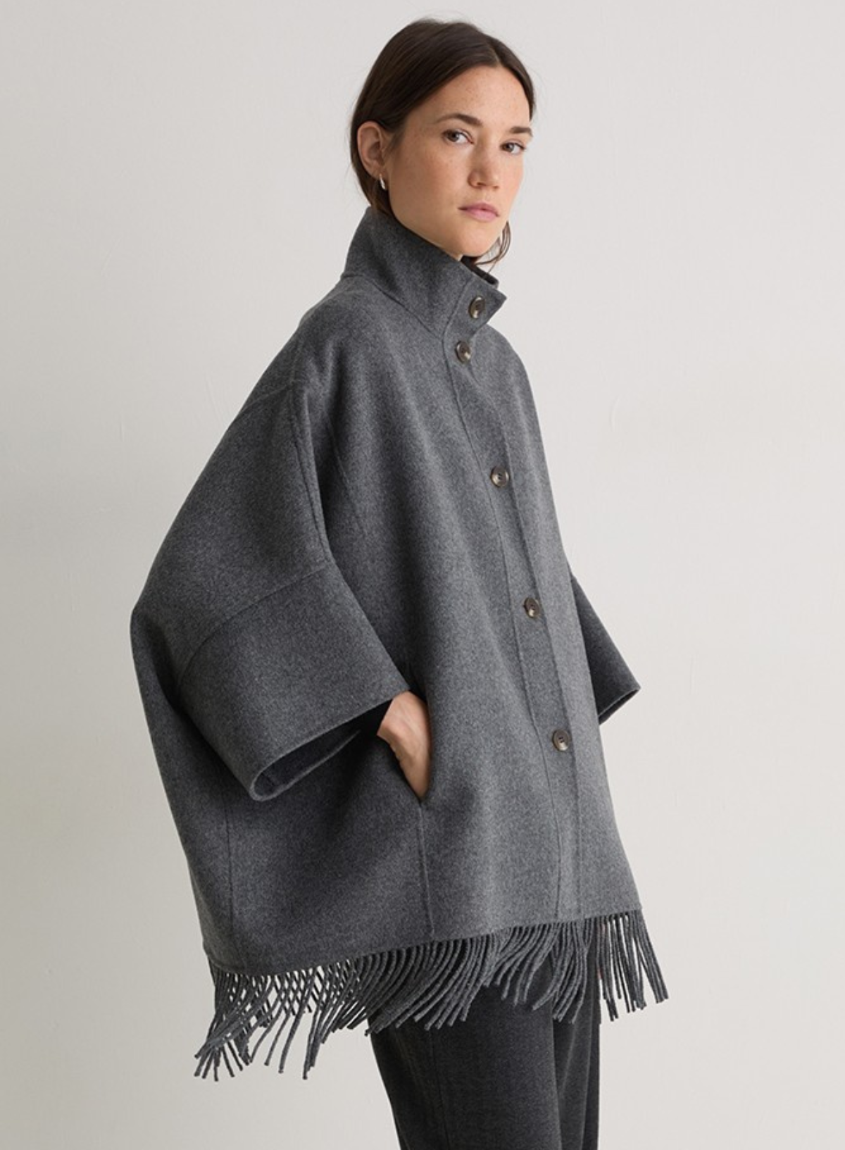 Woman wearing a gray cape with fringes on a plain background