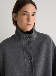 Woman wearing a gray coat with button details against a plain background