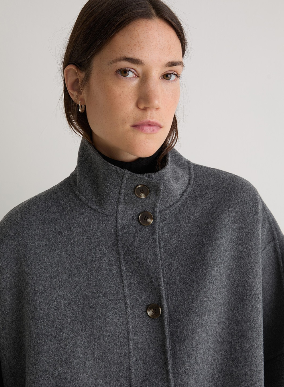 Woman wearing a gray coat with button details against a plain background