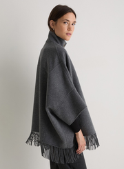 Woman wearing a dark gray poncho with fringes on a plain background