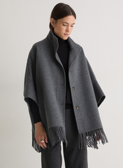 Woman wearing a gray poncho with fringes on a plain background