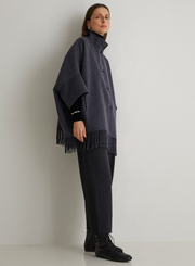 Person wearing a dark gray poncho with fringe standing against a plain background