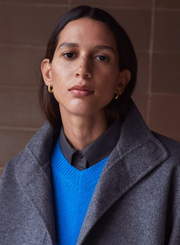 Person wearing a gray coat over a blue sweater with a neutral background
