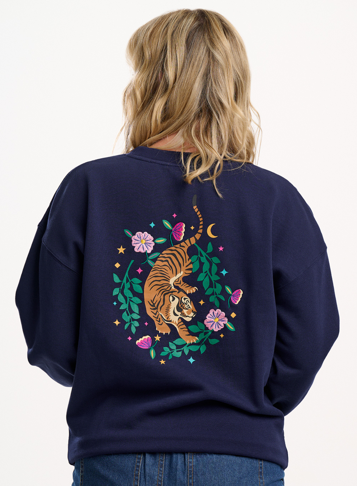 Person wearing a navy blue sweatshirt with a tiger design on the back, standing against a white background.