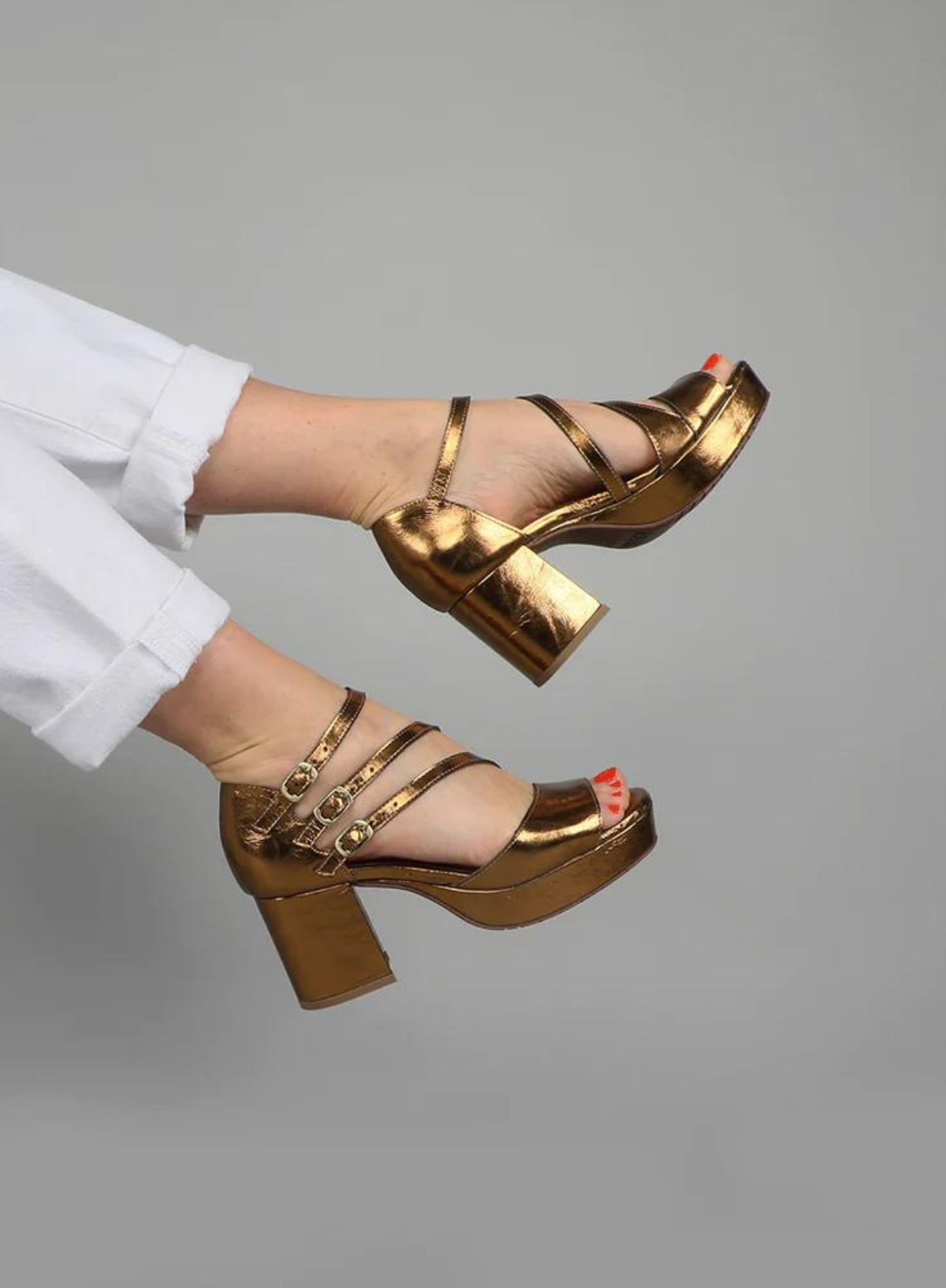 Model wearing the Esska Carmen Bronze Heels styled with white jeans. Model is showcasing the open round toe design and the bronze appearance in side profile.