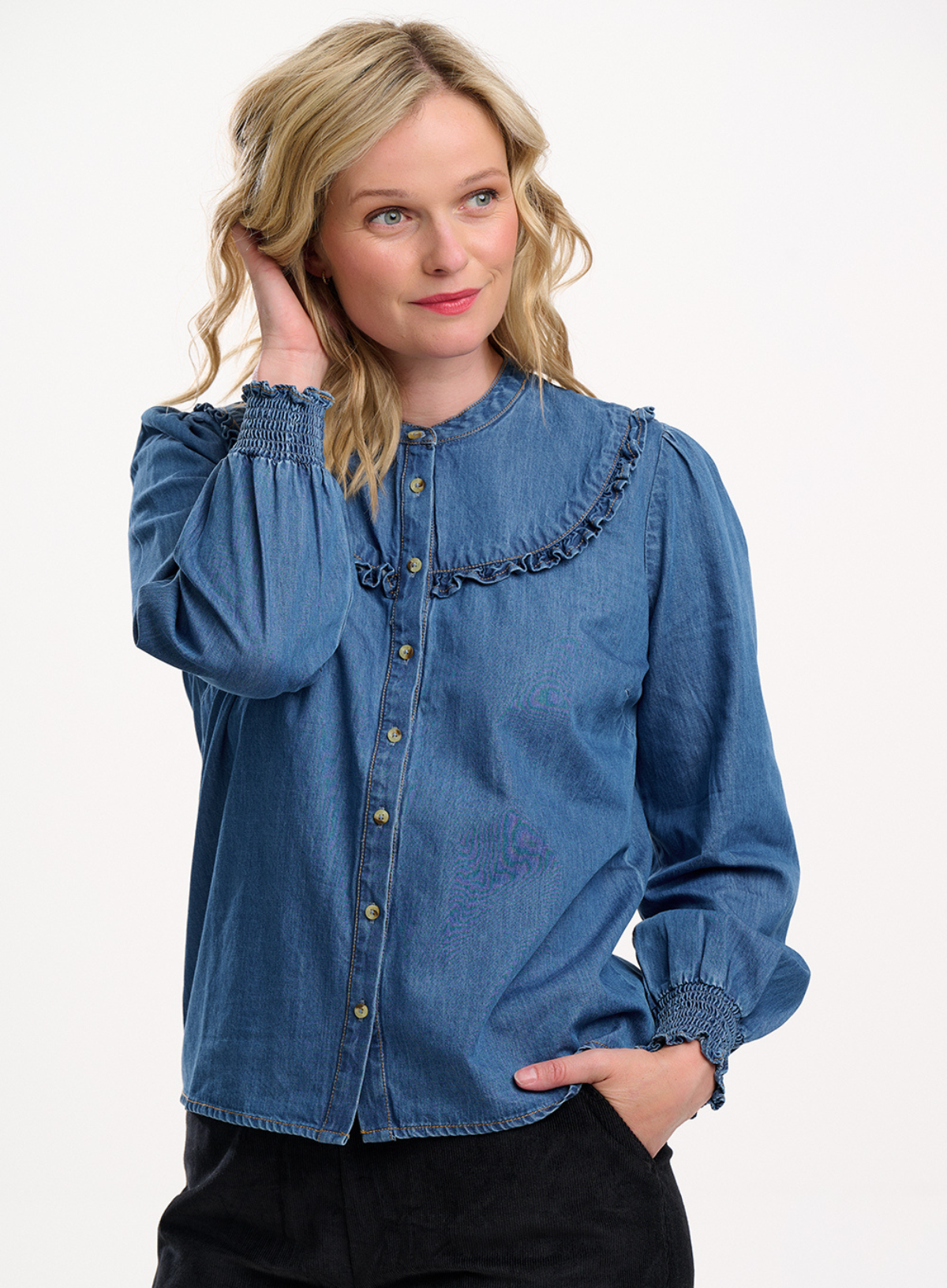 Woman wearing a blue denim blouse with ruffled details on a white background