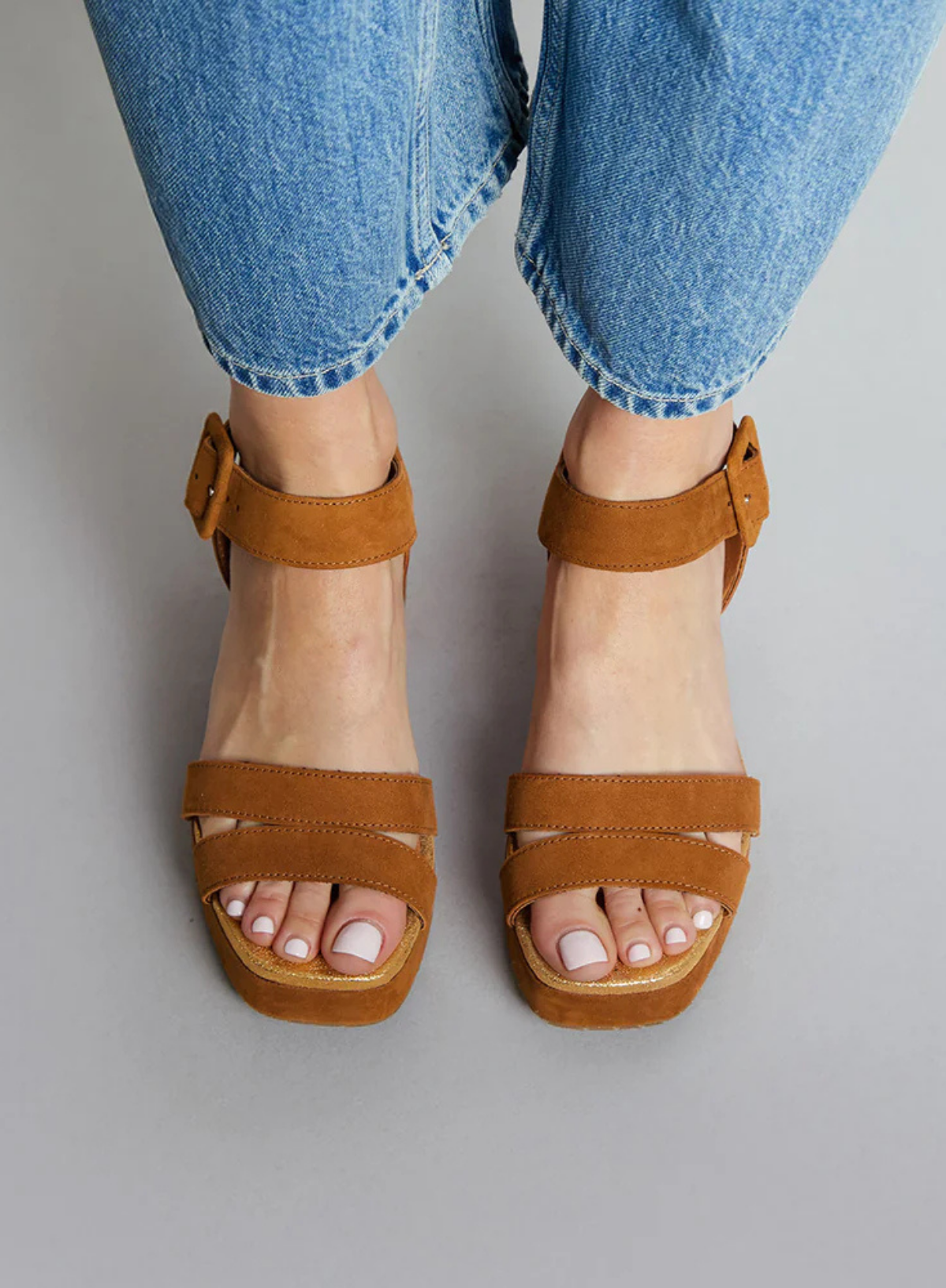 Model wearing the Esska Flora Tan Suede Sandal Heels styled with a pair of light wash denim jeans. Front shot with the model showcasing the round open toe shape of the sandals and their platform height.