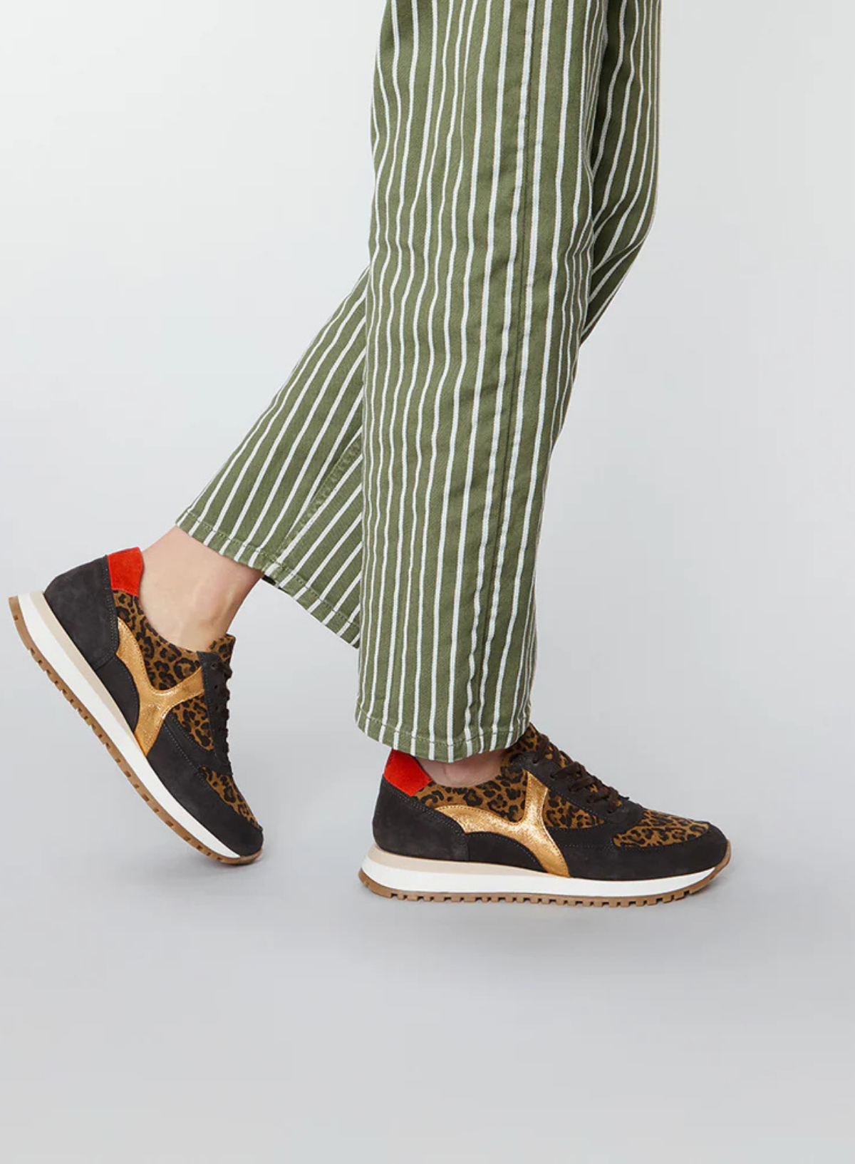 Model wearing a green and white vertical striped jumpsuit styled with the Esska Cinda Animal Print Trainers in side profile showcasing the thicker trainer sole.