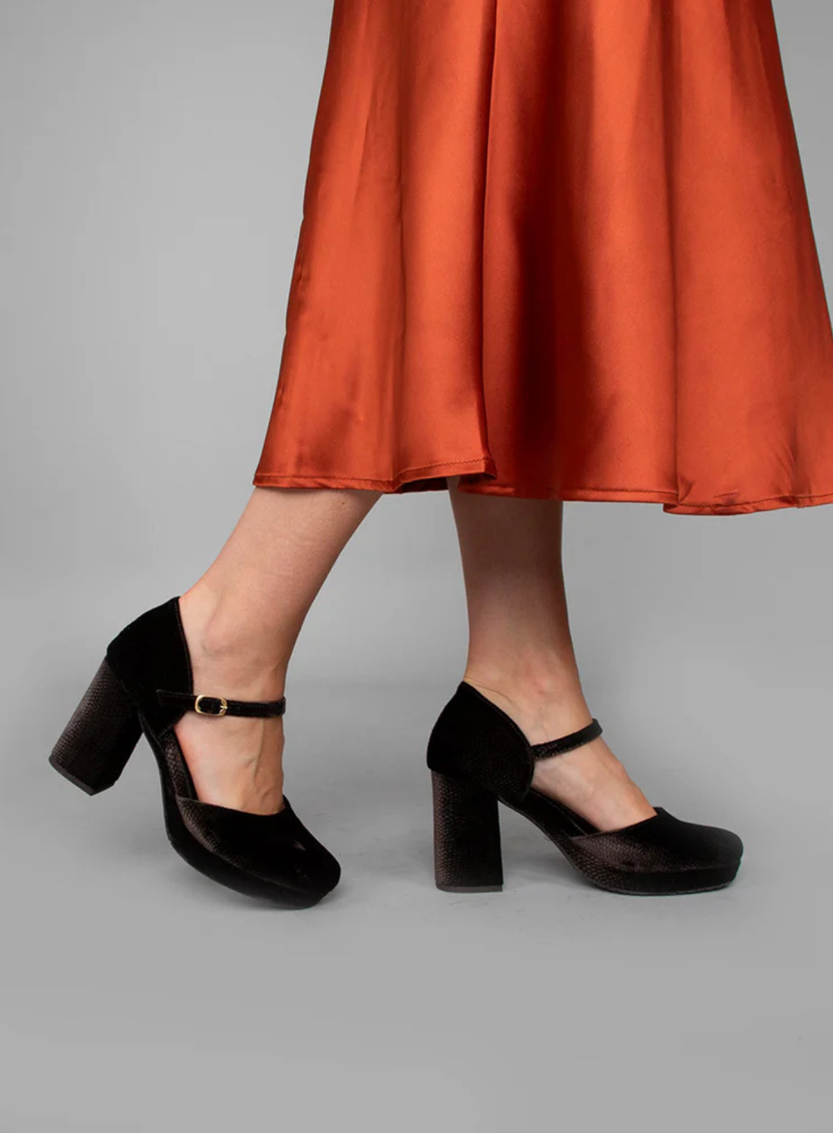 Model wearing the Esska Viv Dark Brown Carbon Velvet Block Heels against a grey backdrop styled with a coral skirt.