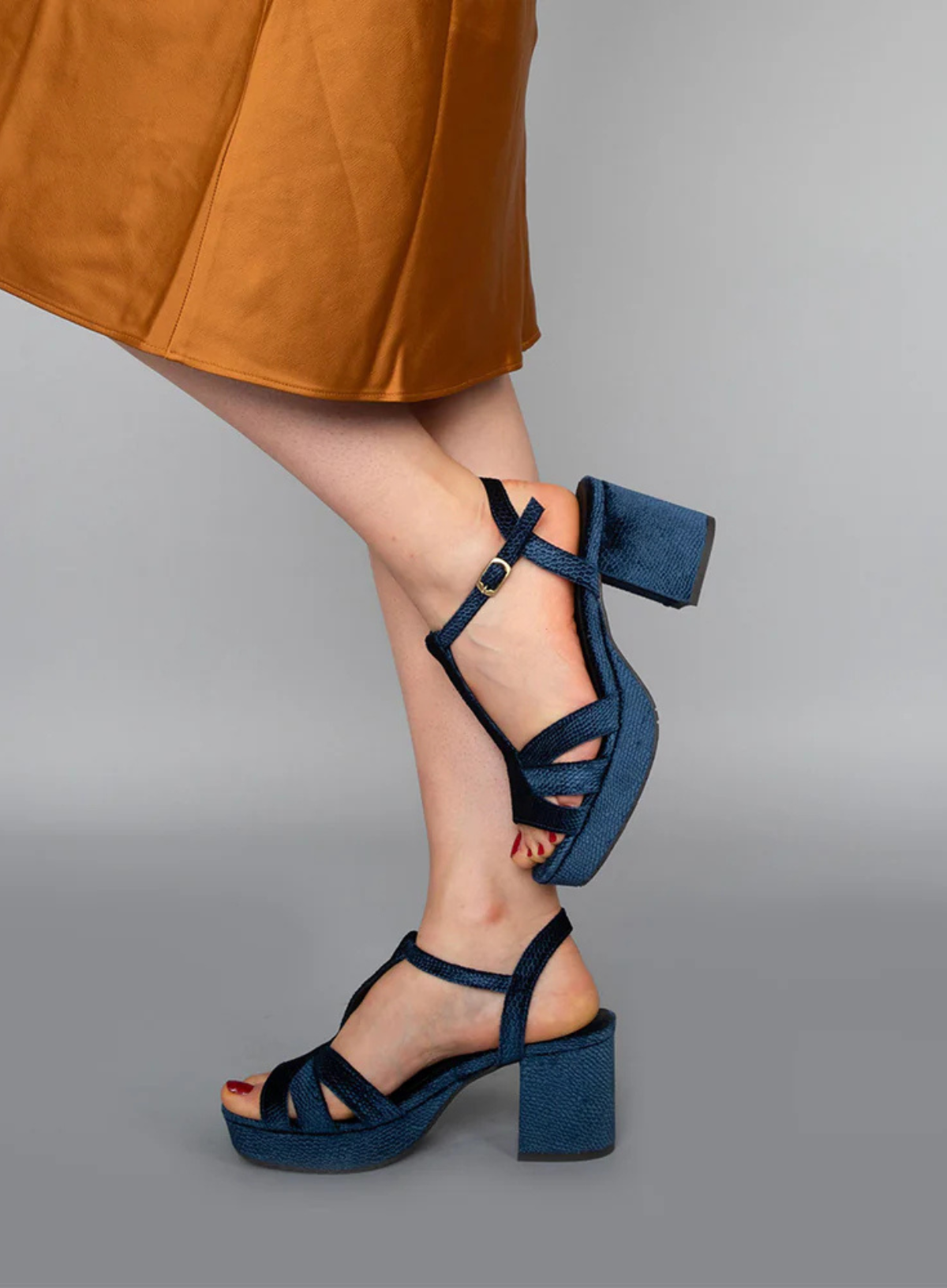 Model wearing the Esska Charlie Blue Velvet T Bar Heels with a burnt orange satin skirt. Model is showcasing the block heel and buckle fasten.