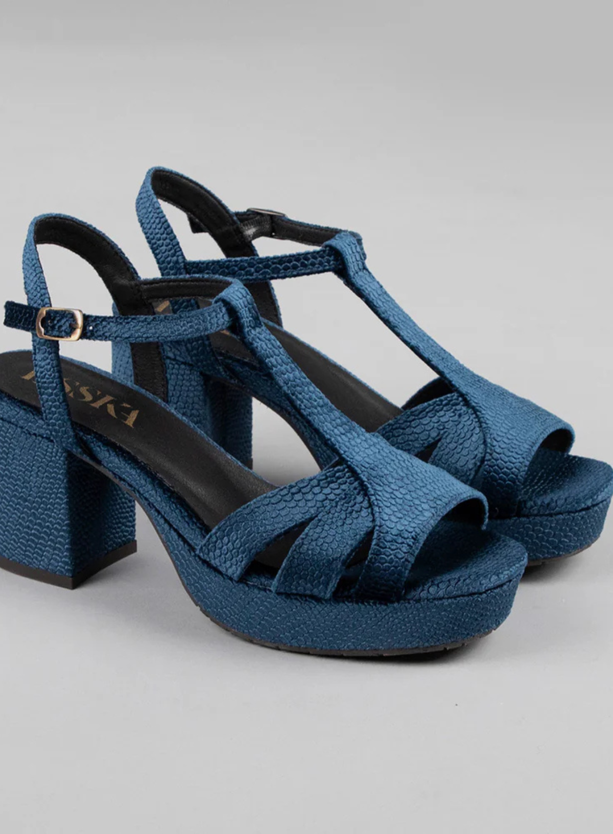 Pair of Esska Charlie Blue Velvet T Bar Heels against a grey background. Close up front side shot showcasing the block heel with embossed velvet lizard pattern and the t bar straps.