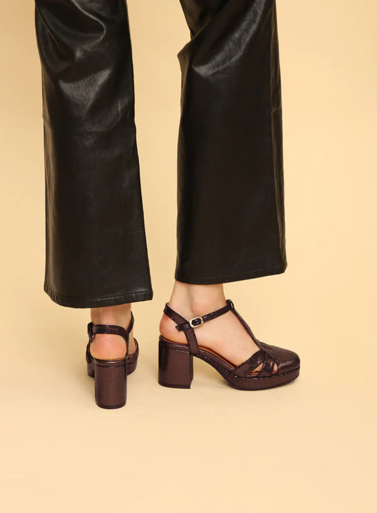 Model wearing the Esska Celeste Dark Brown Metallic Platform Block Heels styled with black leather wide leg cropped trousers. Model is turned away from the camera showcasing the height of the block heels.