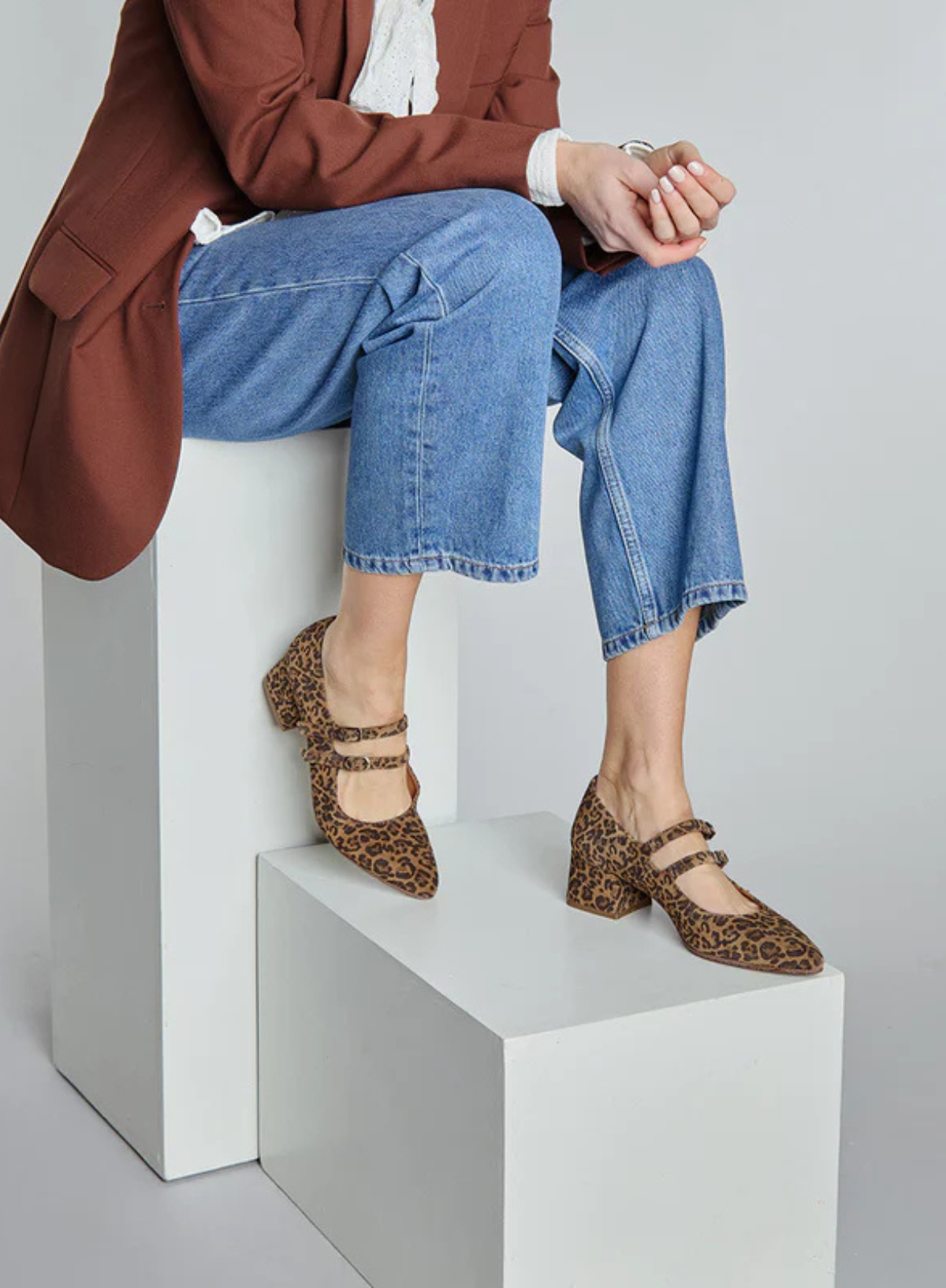 Woman wearing the Esska Laura Low Leopard Heels sitting on a white block with a plain background.