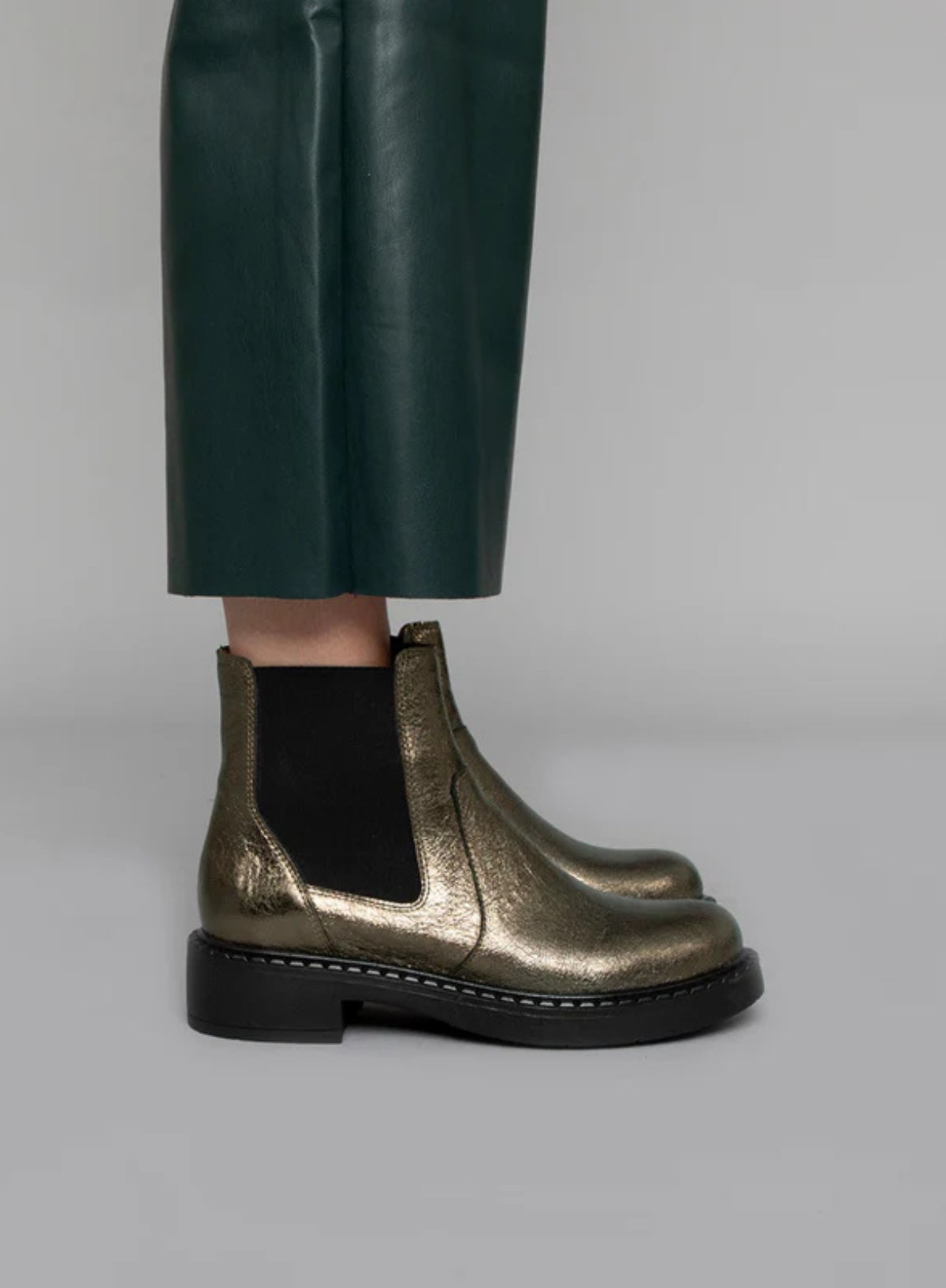 Model wearing the Esska Bora Graphito Leather Chelsea Boots styled with wide leg green leather trousers. Side shot showcasing the round toe shape and the elasticated side panels of these block heeled boots.