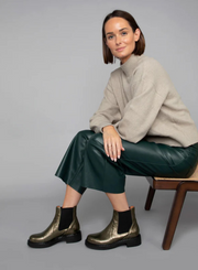Model sitting on a chair wearing a beige sweater, green wide leg leather trousers styled with the Esska Bora Graphito Leather Chelsea Boots against a grey background.