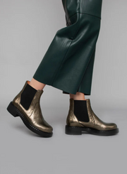 Model wearing the Esska Bora Graphito Leather Chelsea Boots tipping her heel styled with green wide leg leather trousers.