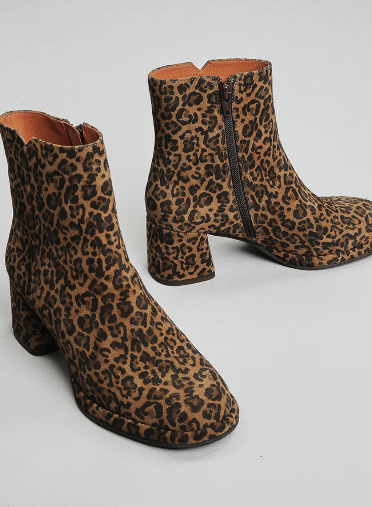 Pair of Esska Mona Leopard Print Boots on a grey background. Front and side shot showcasing the all over leopard print, the round toe shape, side zip closure and the block heel of these ankle boots.