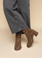 Model wearing the Esska Mona Leopard Print Boots with a pair of charcoal wide leg jeans. Front side shot showcasing the round toe shape, the zip closure and block heel of these leopard print ankle boots.