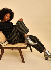 Model shot wearing the Esska Luka Gold Ankle Boots with green and black trousers on with a black jumper sitting on a low chair.