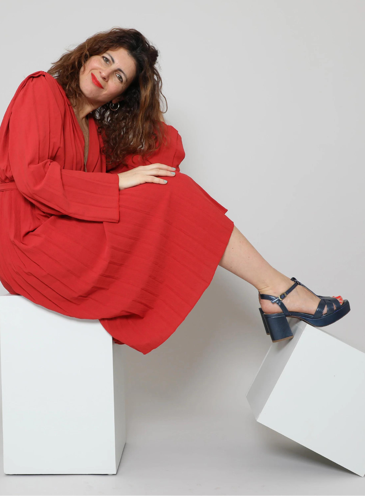 Model wearing a red dress styled with the Esska Charlie Blue T Bar Sandals sitting on a block showcasing the platform soles and block heel.