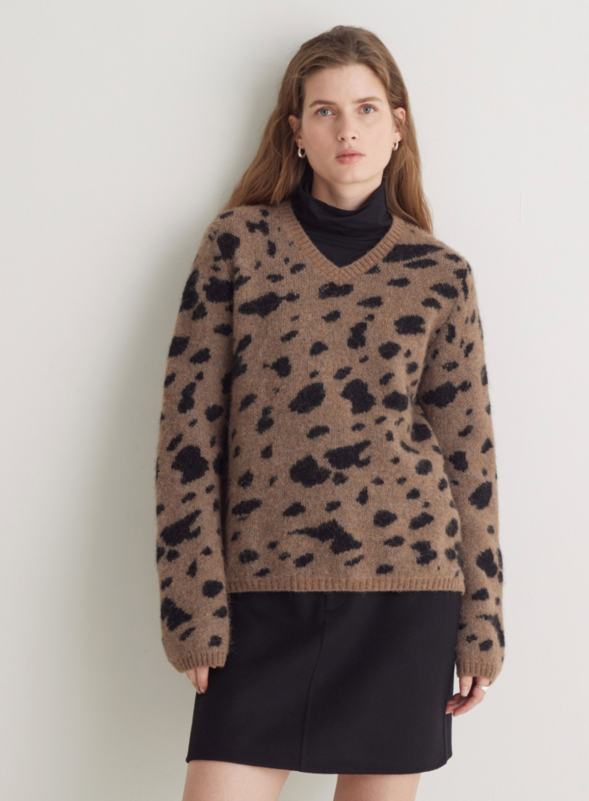 Woman wearing a brown sweater with black spots against a plain background