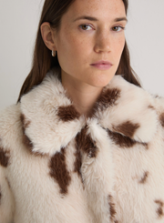 Close-up of a person wearing a fur coat with brown spots on a plain background