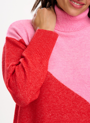 Close-up of a woman wearing the Sugarhill Brighton Winona Pink Red Colour Block Roll Neck Jumper showcasing the ribbed roll neck and sleeve cuffs