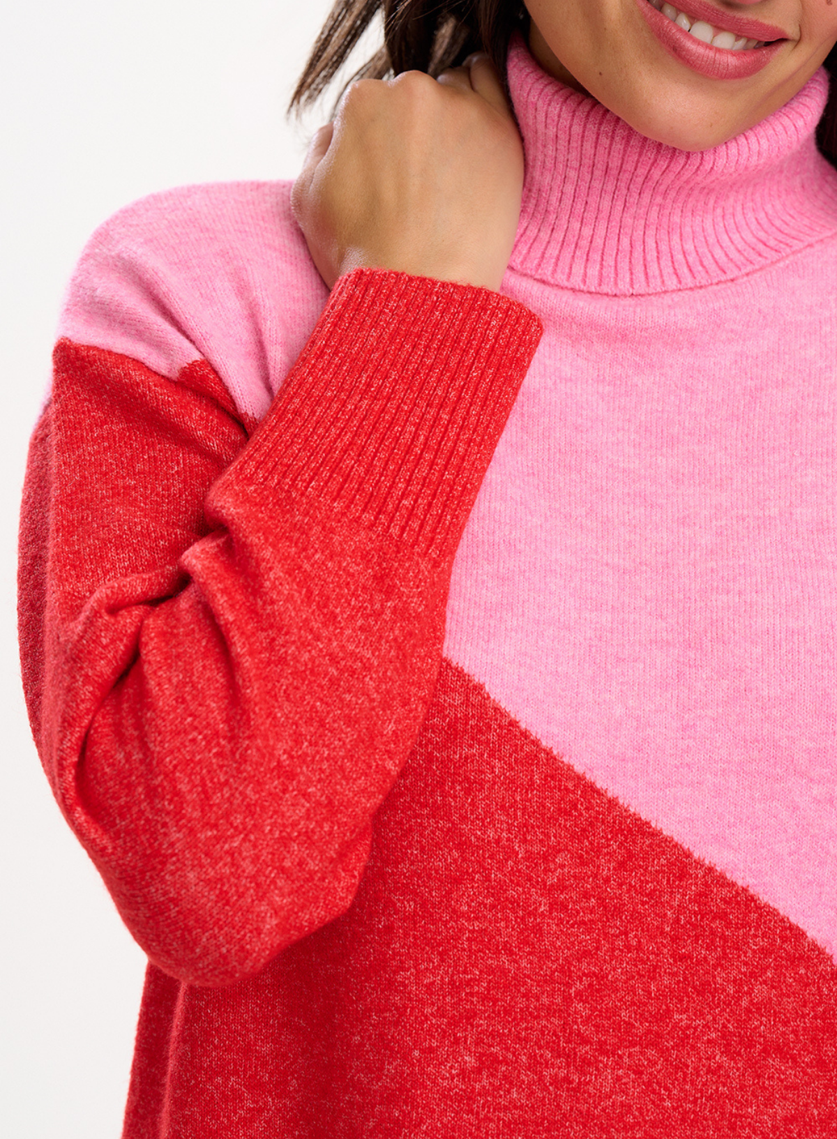 Close-up of a woman wearing the Sugarhill Brighton Winona Pink Red Colour Block Roll Neck Jumper showcasing the ribbed roll neck and sleeve cuffs