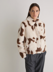 Person wearing a cow print fur coat against a plain background