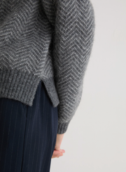 Gray herringbone knit sweater worn by a person on a white background