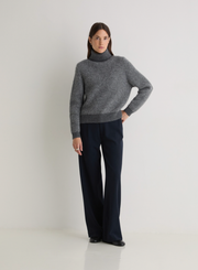 Person wearing a gray sweater and dark pants on a white background