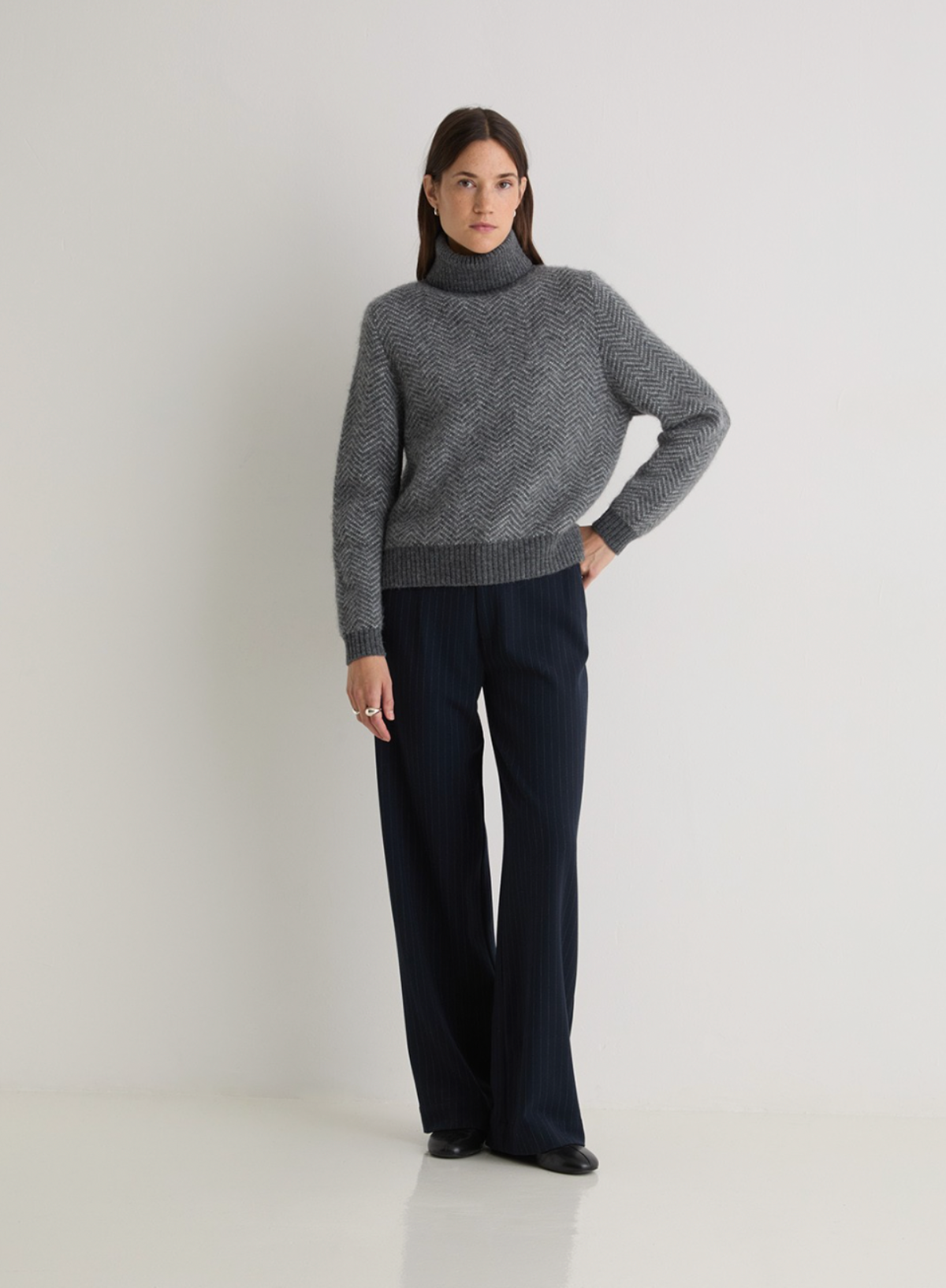 Person wearing a gray sweater and dark pants on a white background