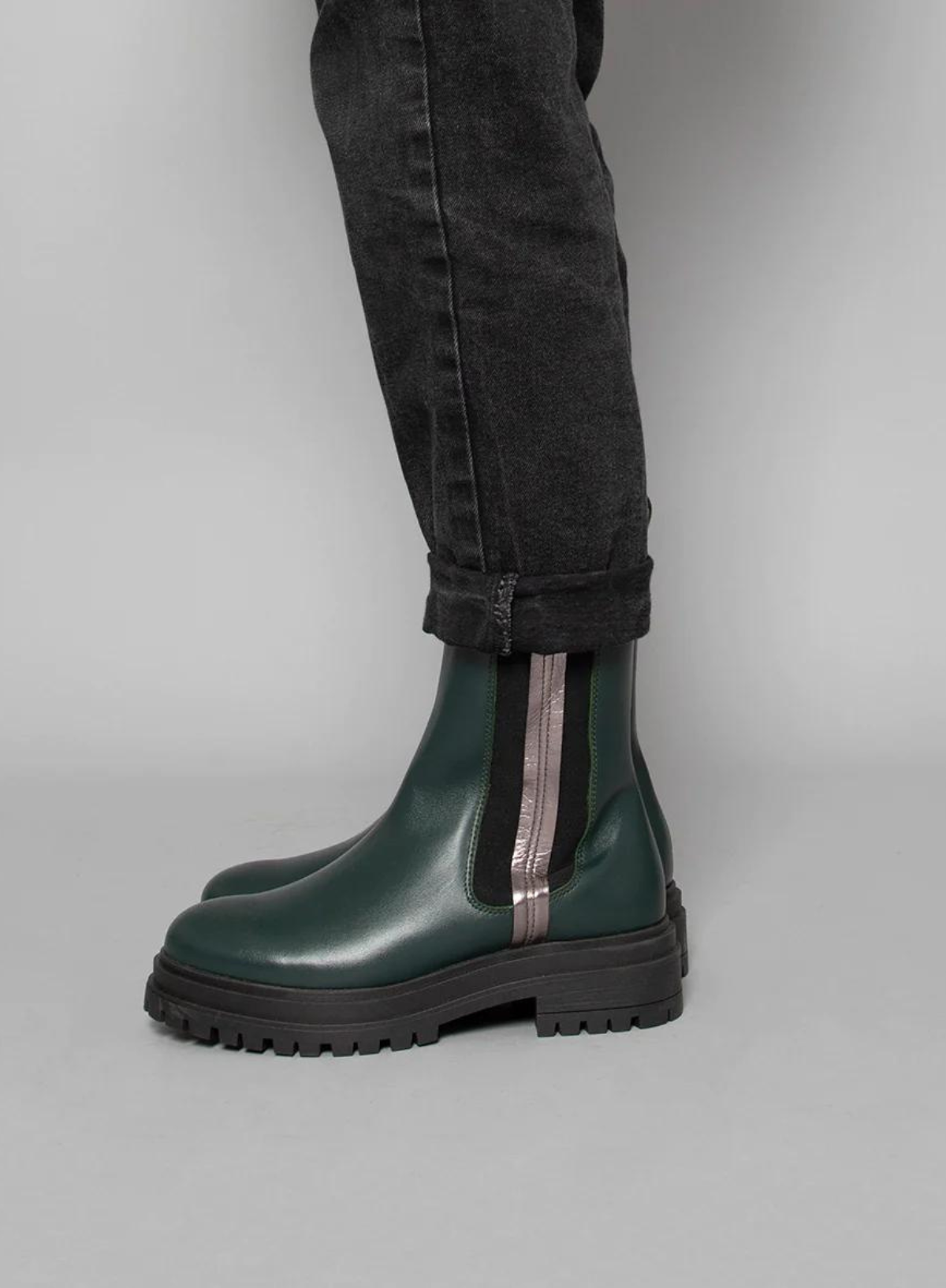 Model wearing a pair of washed black jeans rolled up to the top of the Esska Yaline Green Leather Chelsea Boots against a grey backdrop in side profile.