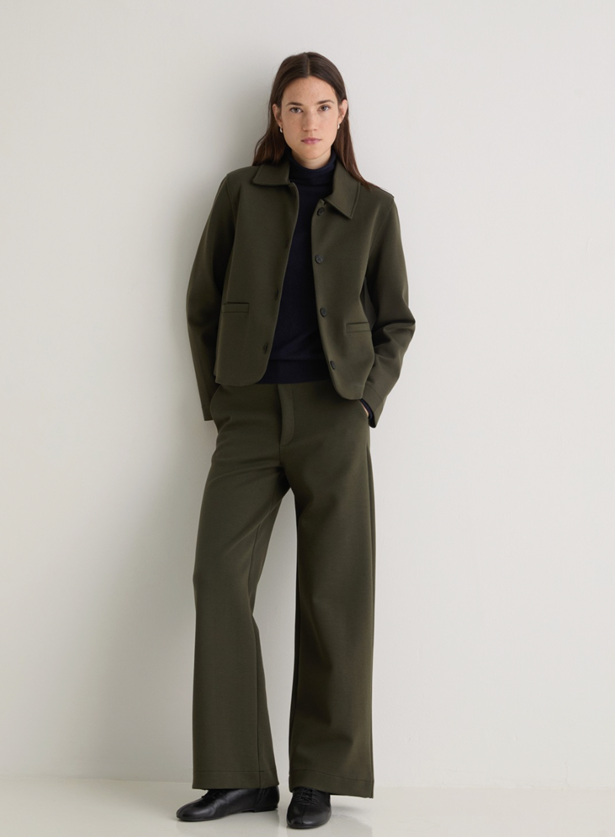 Person wearing a green jacket and trousers on a plain background