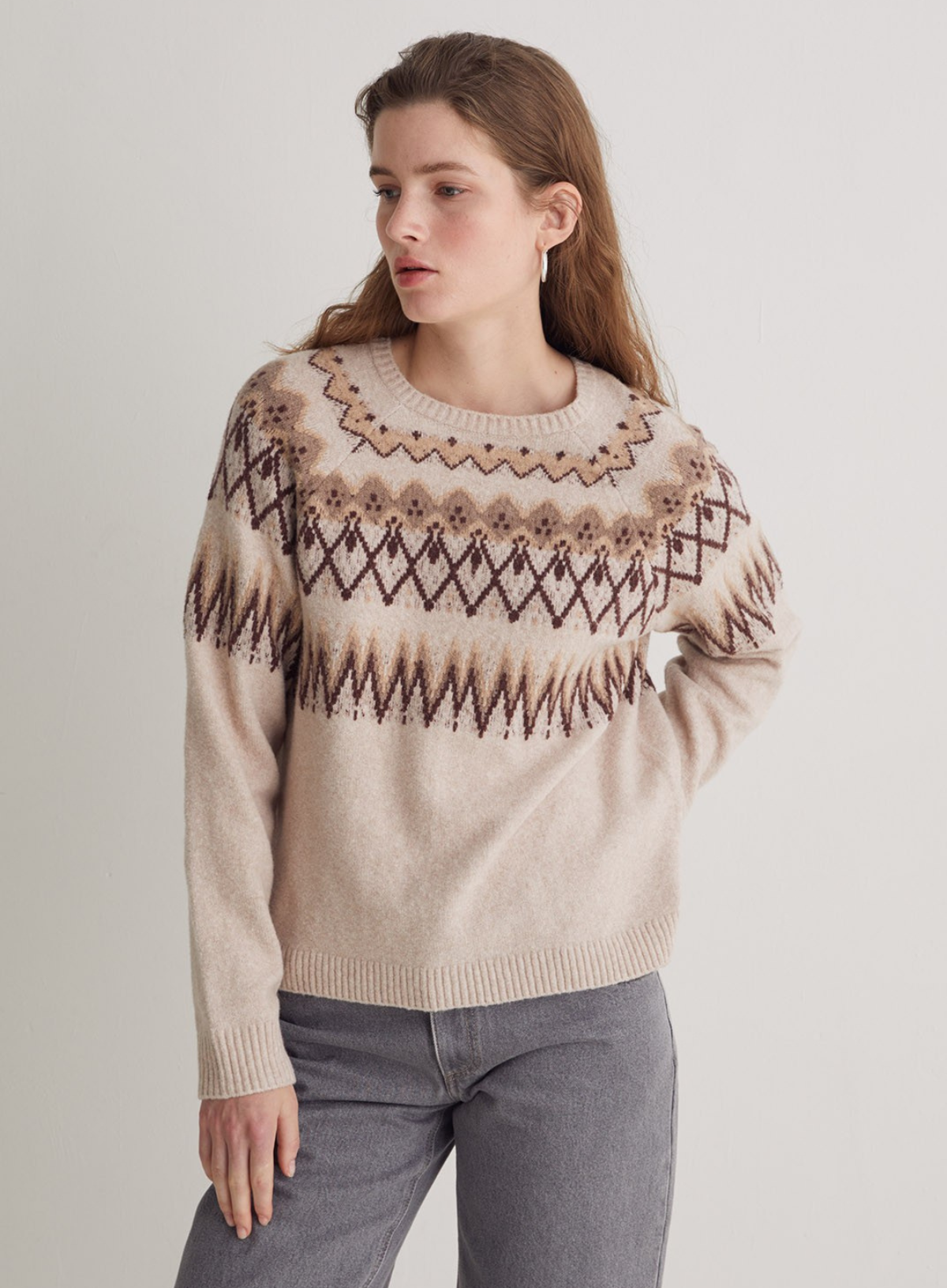 Woman wearing a beige sweater with a pattern on a plain background