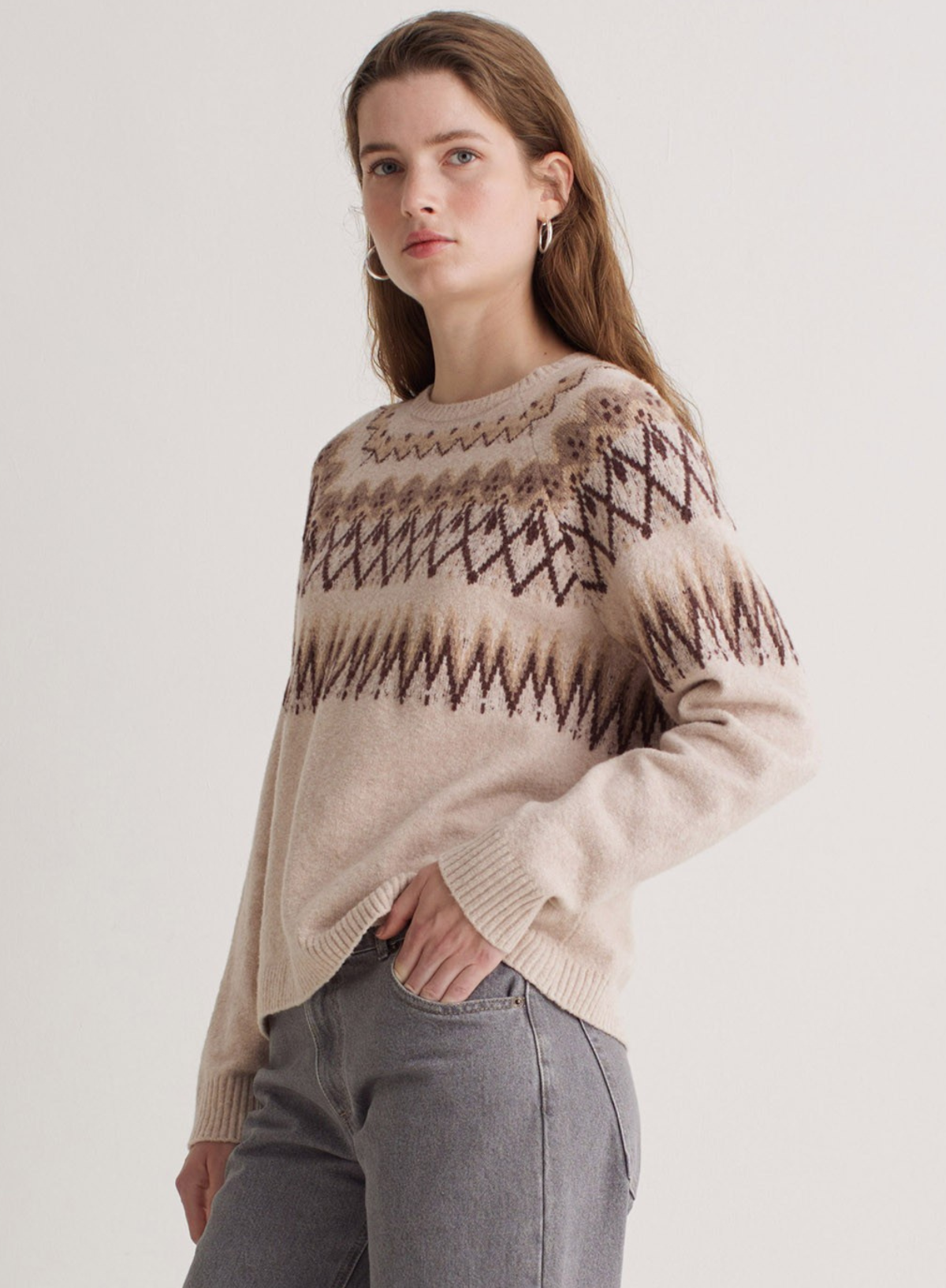 Woman wearing a beige sweater with a pattern on a plain background