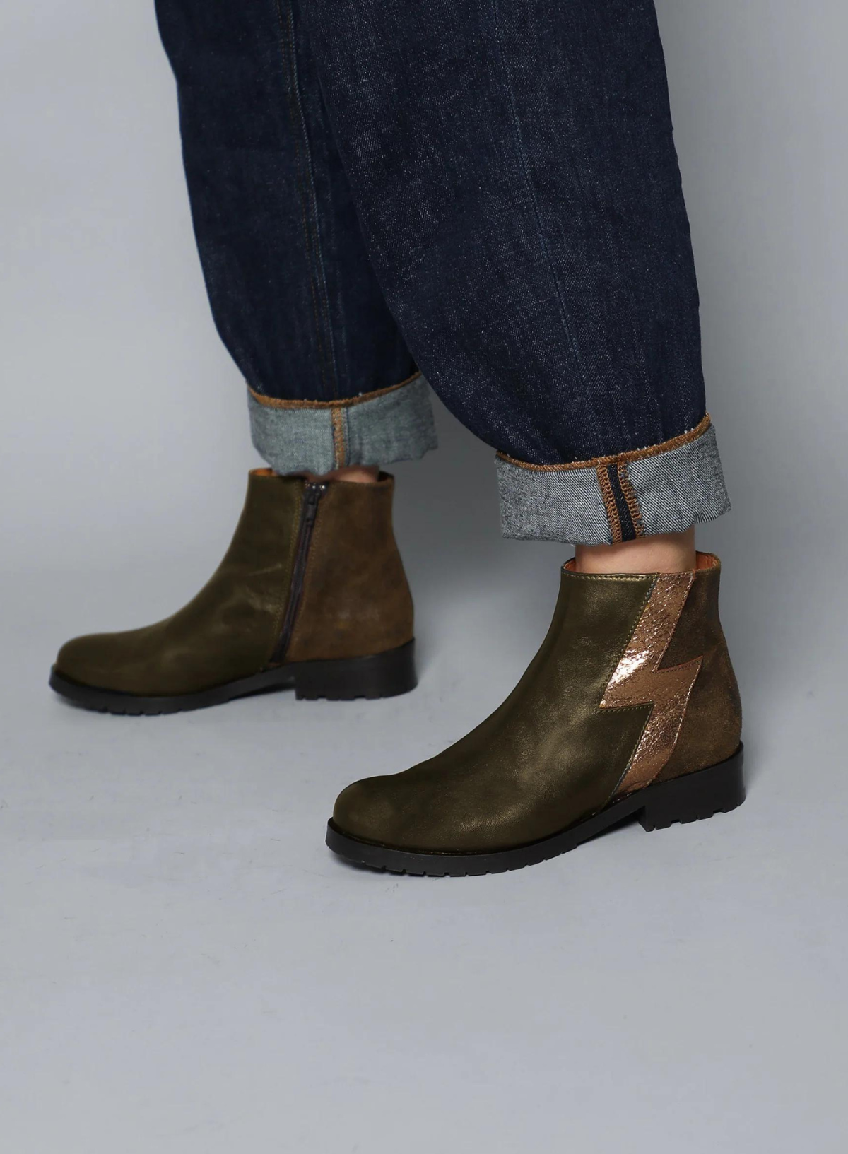 Model wearing the Esska Tatiana Khaki Boots styled with mid wash denim jeans with a turn up. Side profile showcasing the round toe shape and the gold lightning bolt design of the ankle boots.